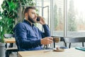 Side view.Young bearded attractive businessman in blue shirt is sitting at wooden table near window in restaurant Royalty Free Stock Photo