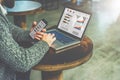 Side view of young bearded businessman sits at round wooden table in cafe and uses laptop with graphs, charts Royalty Free Stock Photo