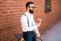 Side view of young bearded man drinking coffee while sitting on his bicycle outdoors Royalty Free Stock Photo