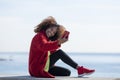 Side view of young beautiful curly african american woman sitting on a bench at beach while using a mobile phone outdoors Royalty Free Stock Photo