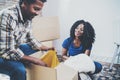 Side view of young black american african couple with moving boxes in new apartment.Cheerful couple sitting in empty new