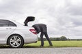 Side view of young businessman looking in trunk of car at countryside