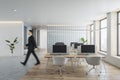 Side view of young businessman walking in modern concrete and wooden coworking office interior with furniture, window and city Royalty Free Stock Photo
