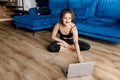 Side view of young caucasian woman fitness trainer hold yoga video lesson at home, show stretching exercise on laptop