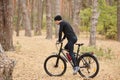 Side view of young European male riding bike in forest on sunny day, sporty man wearing black sportwear and cap onbicycle in wood Royalty Free Stock Photo