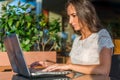 Side view of young female writer writing on her laptop while sitting in park cafe. Girl typing netbook outdoors. Royalty Free Stock Photo