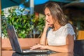 Side view of young female writer writing on her laptop while sitting in park cafe. Girl typing netbook outdoors.