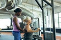 Female trainer assisting active senior woman on lat pulldown machine in fitness studio