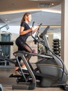 Side view of young fit woman in black elegant lace sport wear on cross fitness stepper. Light gray interior of modern gym Royalty Free Stock Photo