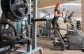 Side view of young fit woman in black elegant lace sport wear on elliptical bike trainer. Light gray interior of modern gym Royalty Free Stock Photo