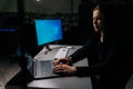 Side view of young hacker man wearing hooded stealing information, preparing to break password sitting at desk in dark Royalty Free Stock Photo