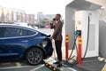 Side view of young handsome african man in business suit, plugging wire into the car socket to charge his new luxury Royalty Free Stock Photo