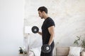 Side view of young handsome man in black sportswear doing biceps curl with dumbbells in living room at home Royalty Free Stock Photo