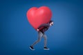 A side view of a young handsome man in a casual outfit carrying a huge red heart on his back. Royalty Free Stock Photo