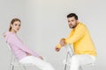 side view of young male and female models in pink and yellow hoodies sitting on chairs and looking at camera Royalty Free Stock Photo