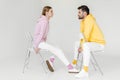 side view of young male and female models in pink and yellow hoodies sitting on chairs and looking at each other Royalty Free Stock Photo