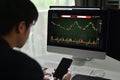 Side view of young male financial analyst using mobile phone and monitoring stocks data candle charts on screen