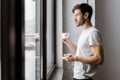 Side view of young man holding cup of coffee and looking at window Royalty Free Stock Photo