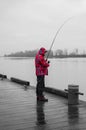 Side view of young man standing on pier with rod. Fisherman in winter fishing on a river