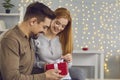 Side view of young married couple unpacking holiday gift together sitting on sofa at home. Royalty Free Stock Photo