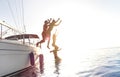 Side view of young millennial friends jumping from sailboat on sea ocean trip - Guys and girls having summer fun together Royalty Free Stock Photo