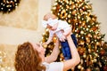 Side view of young mom playing with baby daughter while sitting near Christmas tree in living room Royalty Free Stock Photo