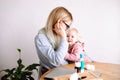 Side view of young mother woman sitting at table, holding little sad baby girl, calming down child at home. Sick time. Royalty Free Stock Photo