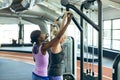 Female trainer assisting active senior woman on lat pulldown machine in fitness studio