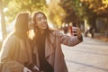 Side view of young, pretty, brunette twin girls making funny faces while taking a selfie with black phone, wearing Royalty Free Stock Photo