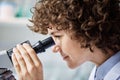 Side view of young serious brunette female biochemist looking in microscope Royalty Free Stock Photo