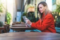 Side view.Young smiling attractive woman in orange coat is sitting outside in cafe at table and uses tablet computer. Royalty Free Stock Photo