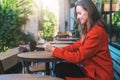 Side view.Young smiling attractive woman in orange coat is sitting outside in cafe at table and uses tablet computer. Royalty Free Stock Photo