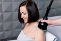 Side view of young smiling woman getting electric massage on her shoulders and neck in the spa. Hardware cosmetology Royalty Free Stock Photo