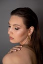 Side view of young stunning woman with long dark hair, golden make-up, earrings with closed eyes, touching shoulder.