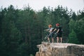 side view of young trial bikers standing on rocky cliff with blurred pine forest on background Royalty Free Stock Photo