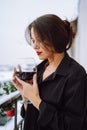 Side view of young woman with dark hair wear black shirt, standing on balcony, holding glass of red wine, closing eyes. Royalty Free Stock Photo