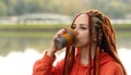 Side view of young woman drinking coffee. Female with redheads dreadlocks with a cup of coffee or tea on background of