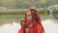 Side view of young woman drinking coffee. Female with redheads dreadlocks with a cup of coffee or tea on background of