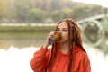 Side view of young woman drinking coffee. Female with redheads dreadlocks with a cup of coffee or tea on background of