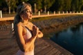 Side view of young woman holding hands in namaste gesture standing by water in soft sunlight at summer sunset. Royalty Free Stock Photo