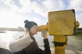 Side view of young woman in hooded sweatshirt looking through telescope by river Thames, London, UK Royalty Free Stock Photo