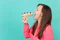 Side view of young woman in knitted pink sweater with closed eyes hold in hand, eating eclair cake isolated on blue