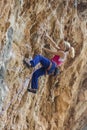 Side view of the young woman rock climber in bright blue pants climbing on the vertical challenging rock wall