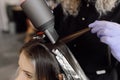 Side view of young woman sitting in beauty salon. Unrecognizable woman colorist drying strand of dyed hair using dryer.