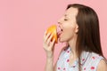 Side view of young woman in summer clothes holding in hand, licking half of fresh ripe grapefruit isolated on pink Royalty Free Stock Photo