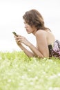 Side view of young woman text messaging through cell phone while lying on grass against clear sky Royalty Free Stock Photo