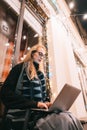 Side view of young woman using laptop on street with night city Royalty Free Stock Photo