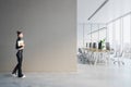 Side view of young woman walking in modern light concrete coworking office interior with blank mock up place on wall, panoramic Royalty Free Stock Photo