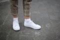 Side view of young women`s foot in white sneakers on asphalt background.