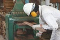 Side view of young wood worker in white safety uniform working with planing machine in factory.